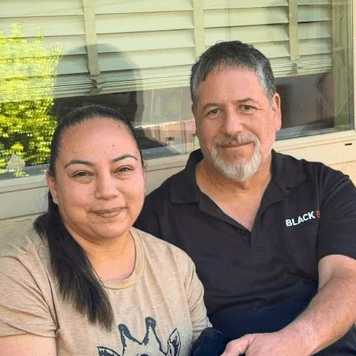 Smiling woman and man sit close together on a porch, posing for a photo.